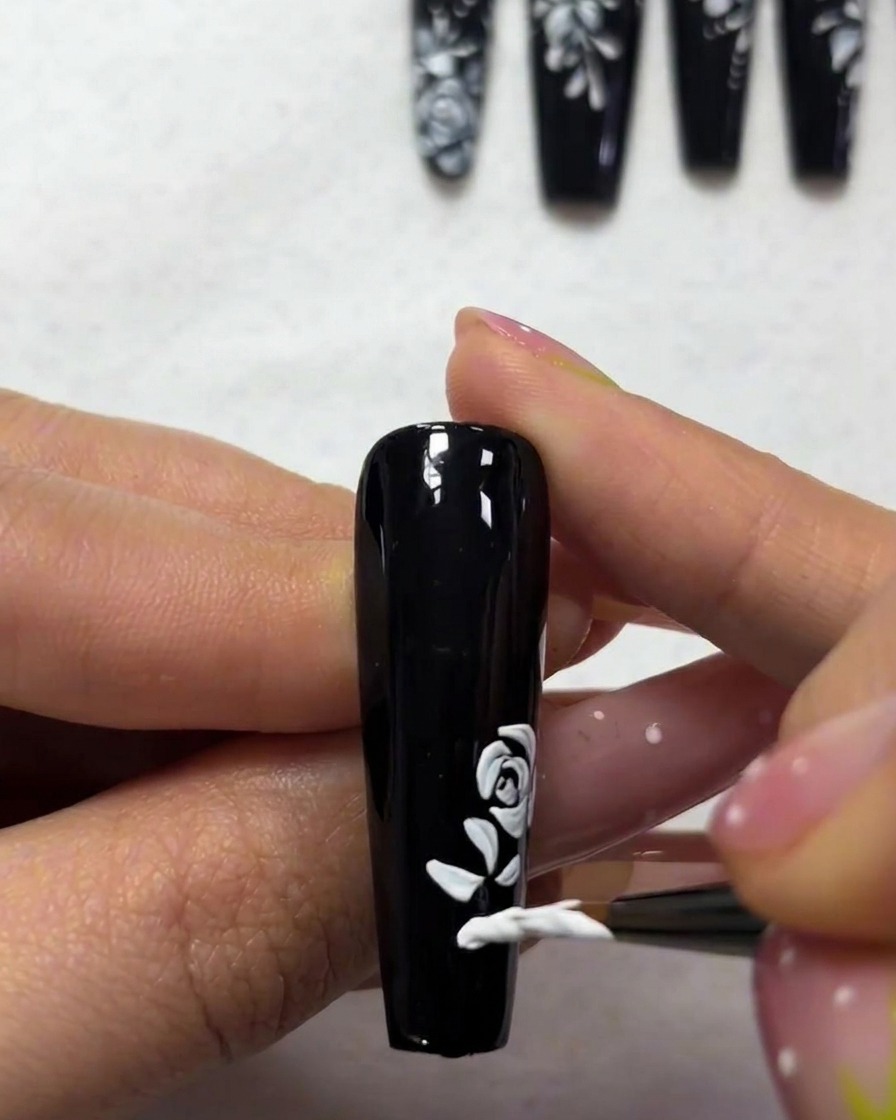 Primer plano que muestra un pincel fino pintando pequeñas hojas blancas puntiagudas cerca de la base de un diseño de rosa.