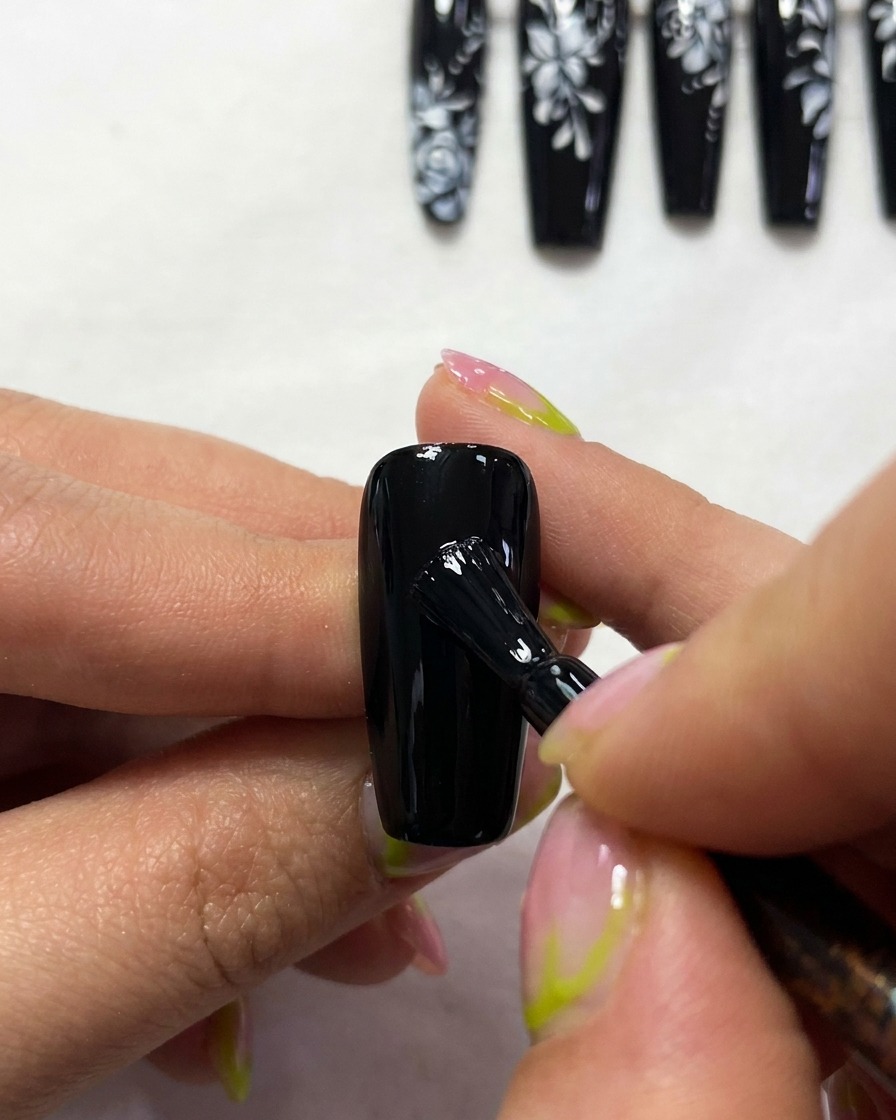 Primer plano de un pincel pintando los contornos blancos finos y elegantes de una estructura de ala de mariposa sobre una uña negra.