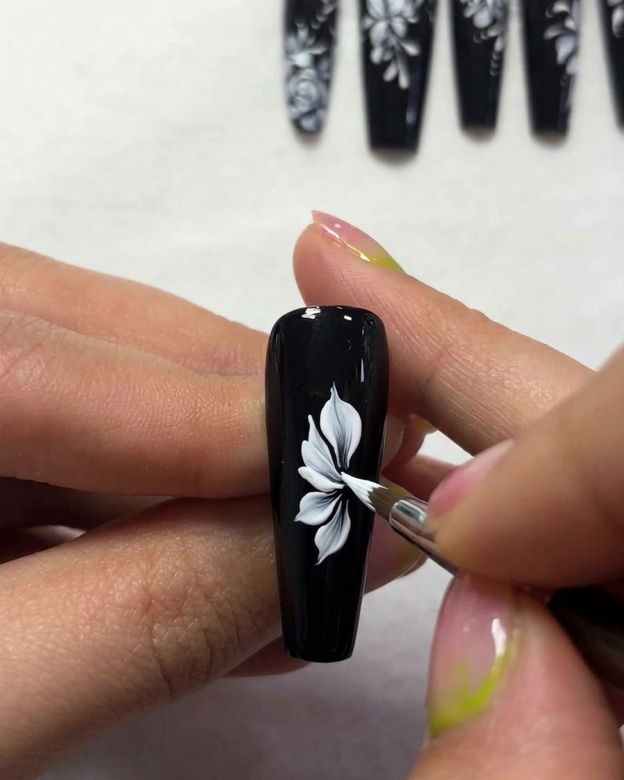 Primer plano de un pincel creando contornos de alas de mariposa blancas, finas y elegantes sobre una superficie de uña negra.