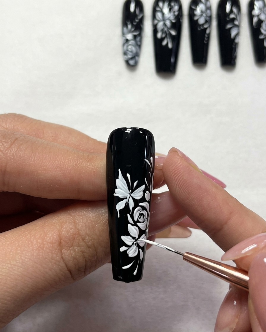 Primer plano de un pincel de detalle añadiendo pequeños puntos blancos a un diseño floral sobre base negra.