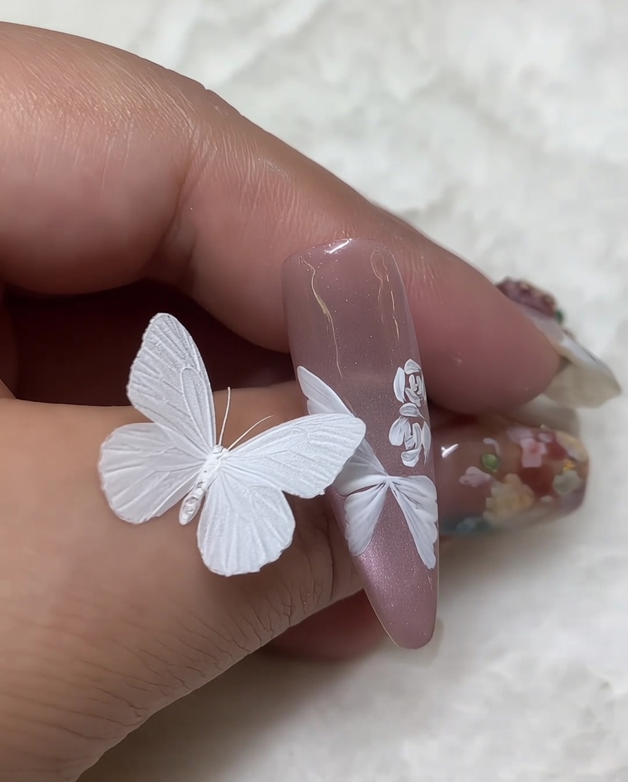 Toma macro del detalle de un diseño terminado de uña con rosa blanca donde se ha profundizado el centro con trazos pequeños y densos de pintura blanca.