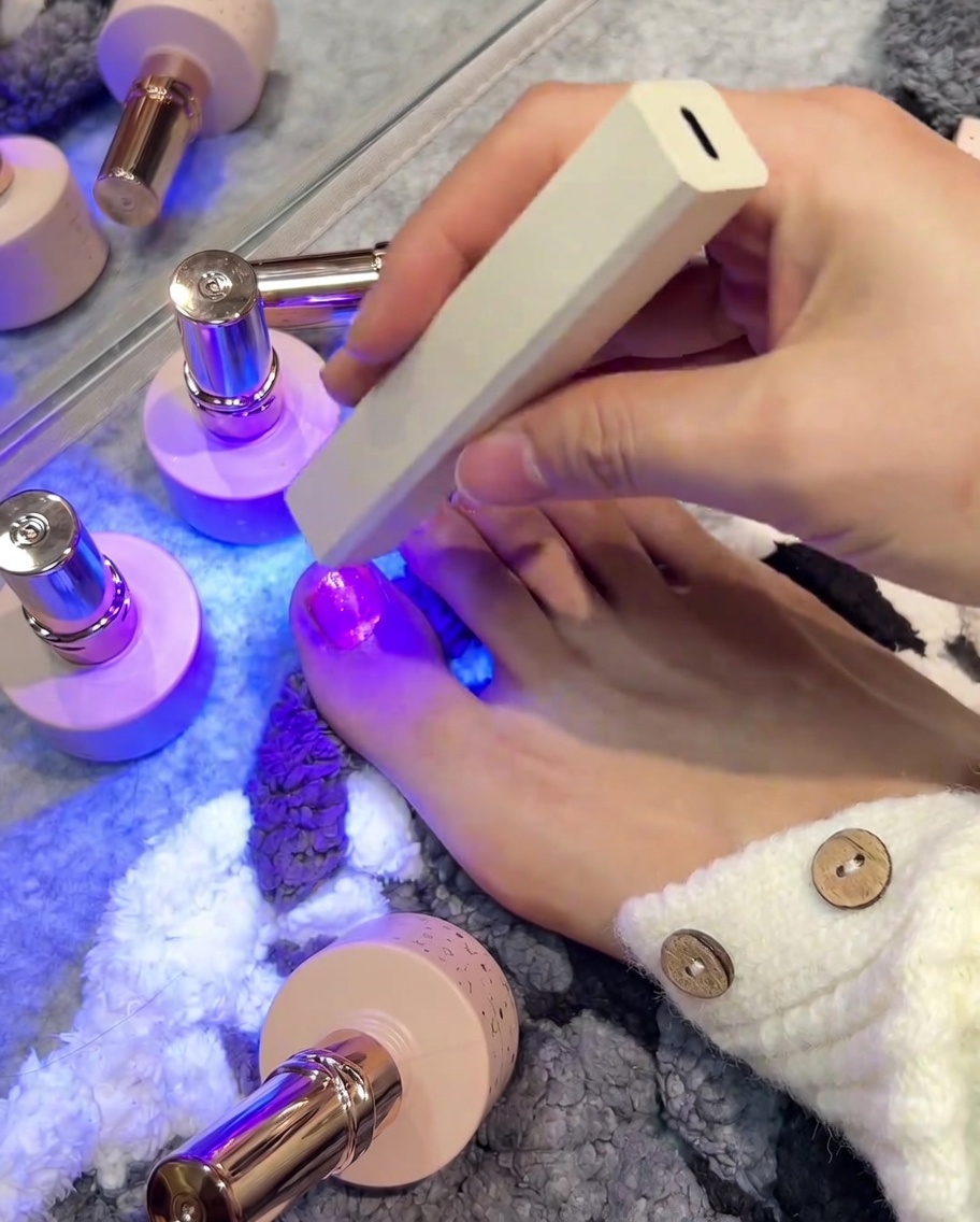 Mano sosteniendo una pequeña lámpara UV/LED sobre una uña recién esmaltada.