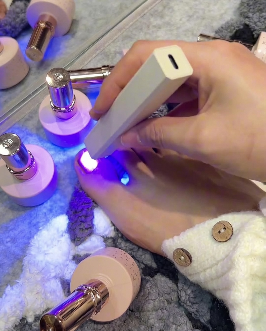 Pincel aplicando esmalte gel oro rosa en una uña más pequeña.