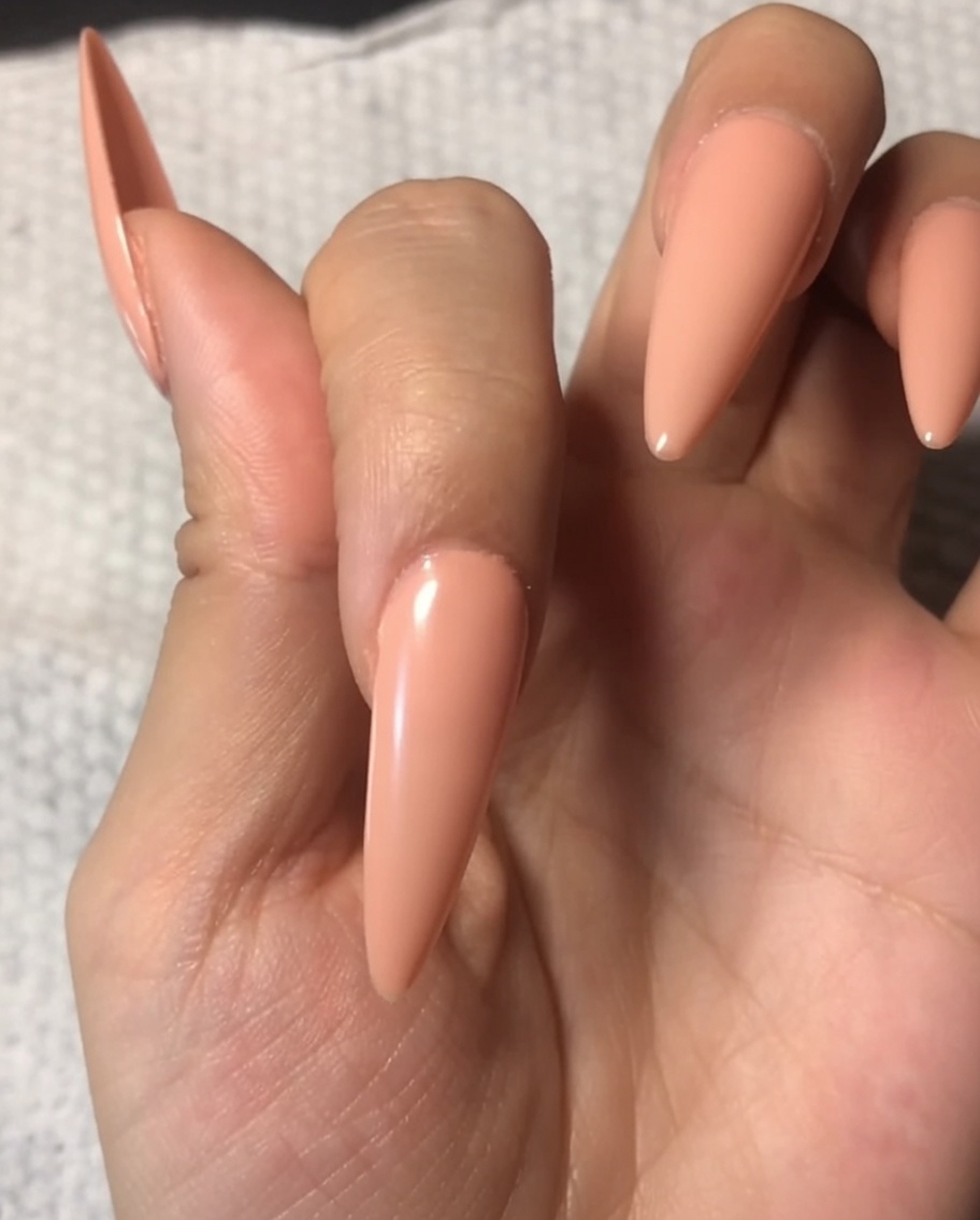 Un pincel aplicando una capa superior transparente y brillante sobre una uña ya pintada con una base nude suave.