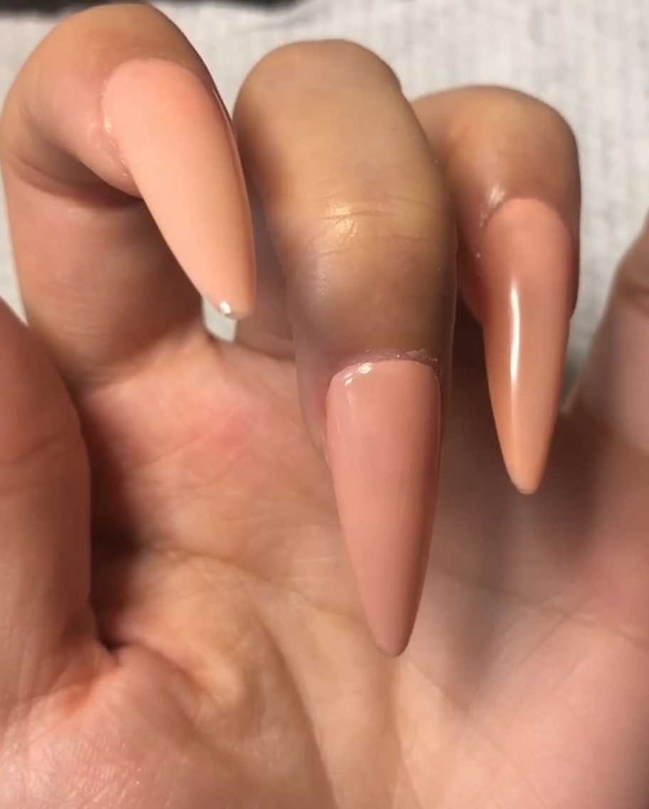 Un pincel de uñas aplicando una capa fina de top coat sobre el gel nude en el dedo índice.