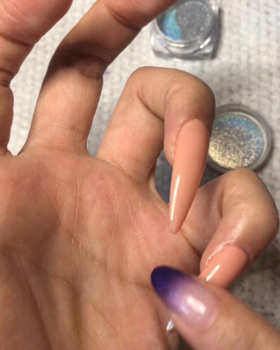 La yema de un dedo limpia difuminando suavemente el borde del polvo holográfico hacia arriba sobre la uña nude para crear un degradado ombré sin costuras.