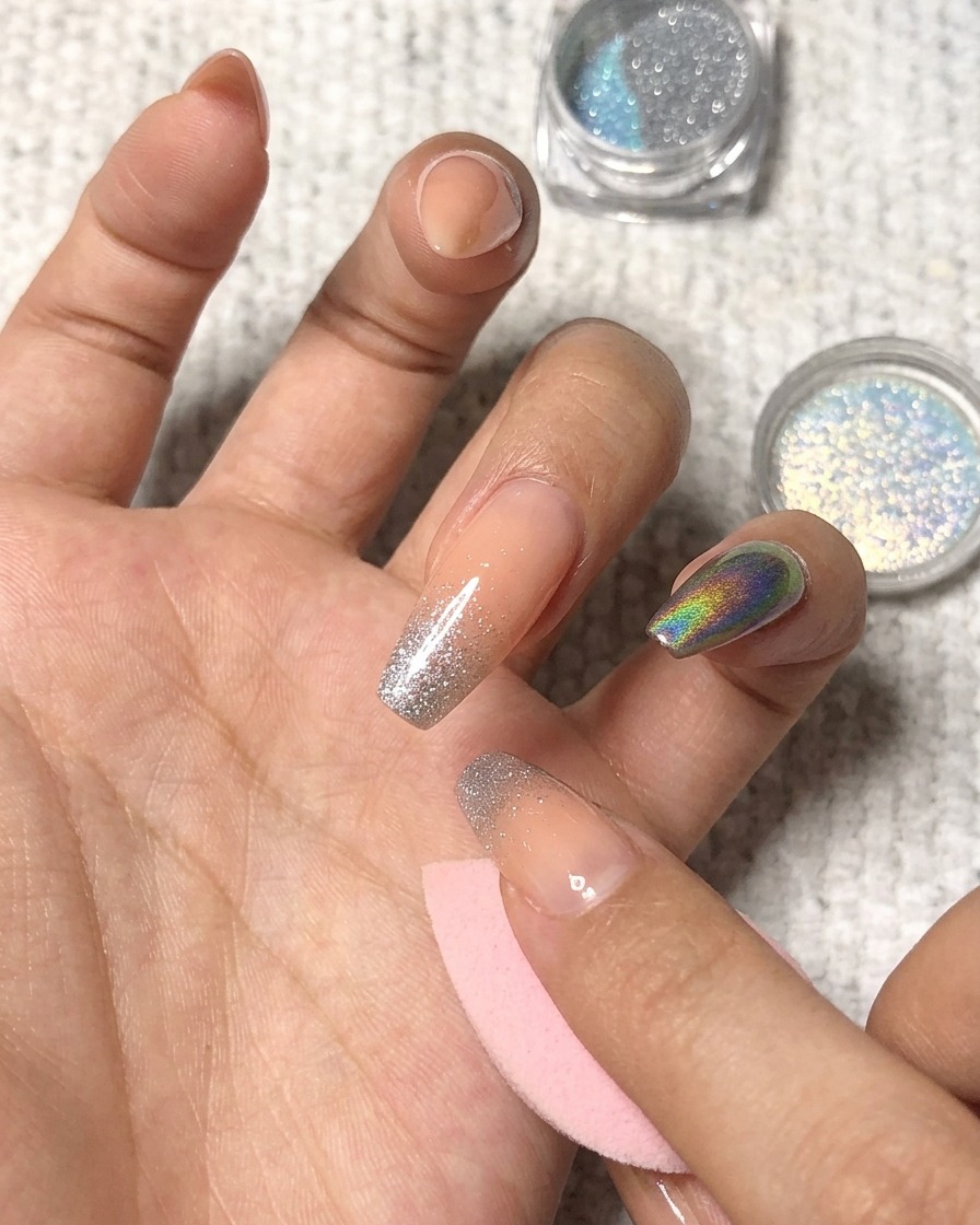 Aplicando polvo holográfico a toques sobre la punta de un dedo anular manicurado.