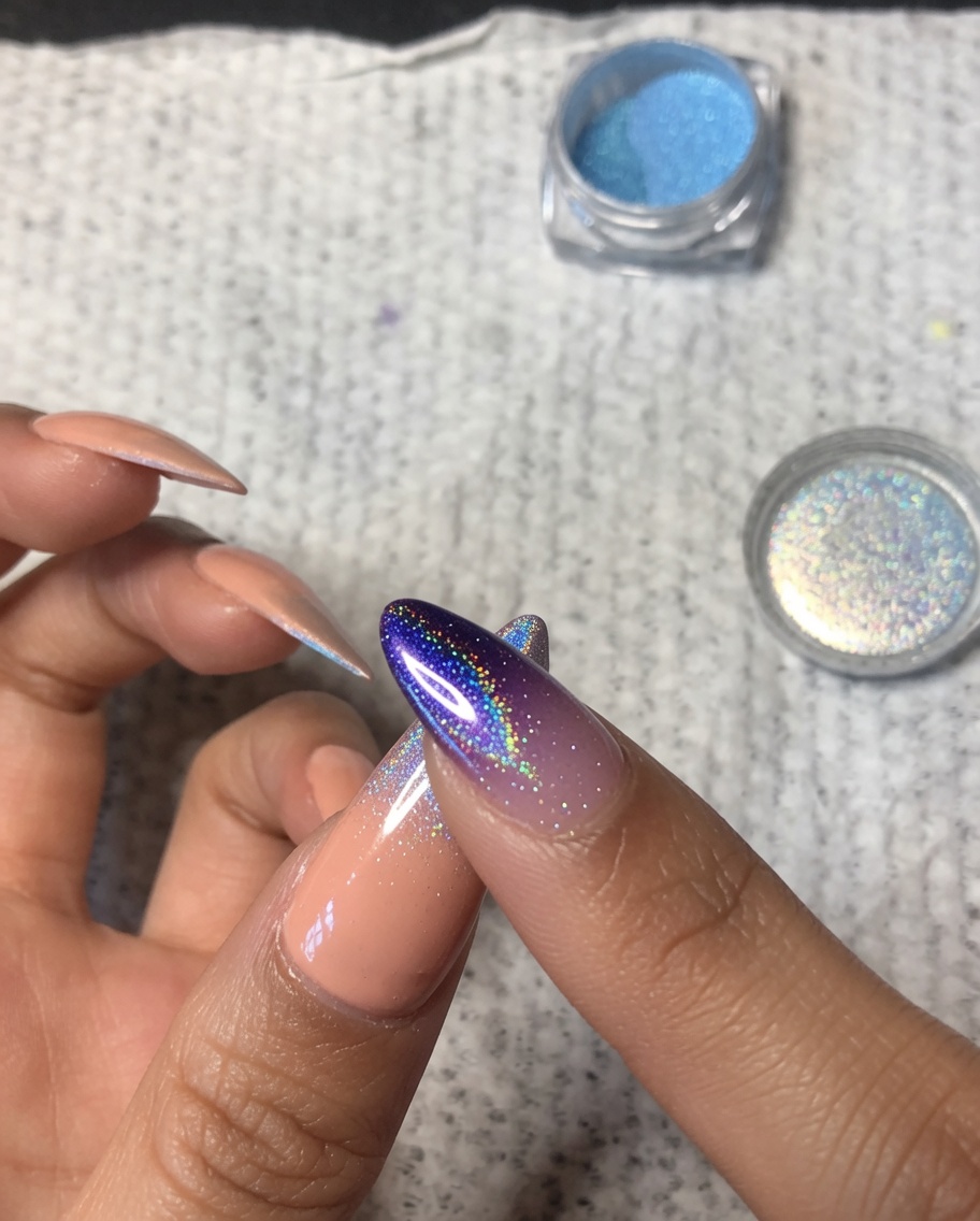 Primer plano de un dedo difuminando suavemente polvo cromado holográfico sobre el centro de una uña del pulgar para crear un desvanecido ombré suave.