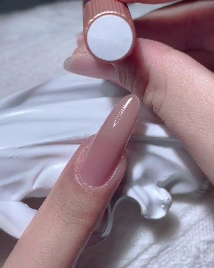Una mano sosteniendo un frasco de esmalte de gel color nude.