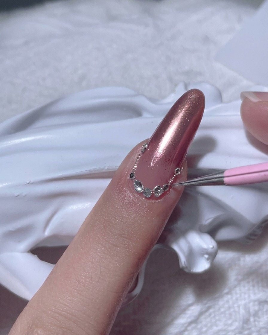 Un punzón colocando un diamante de imitación transparente en la uña cerca de la cutícula.