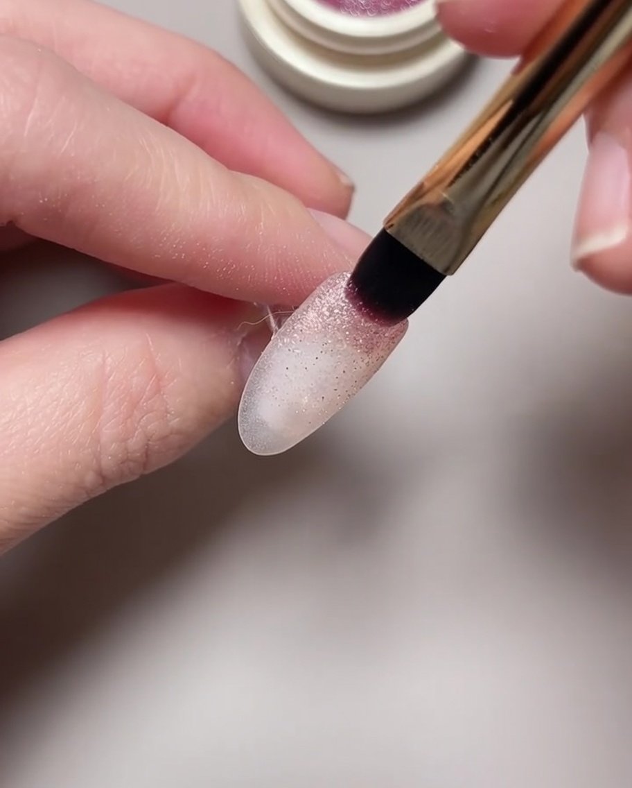 Primer plano de un imán siendo pasado sobre un esmalte de ojo de gato húmedo para formar un patrón de nebulosa.