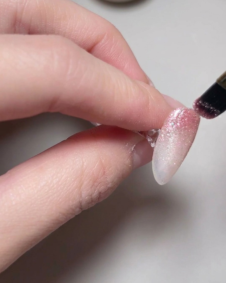 Una mano posicionada dentro de una lámpara con esmalte de uñas ojo de gato curándose.