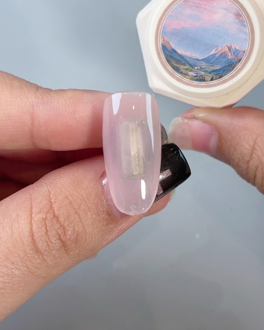 Un pincel de uñas aplicando un top coat transparente sobre una uña cromada con acabado de espejo.