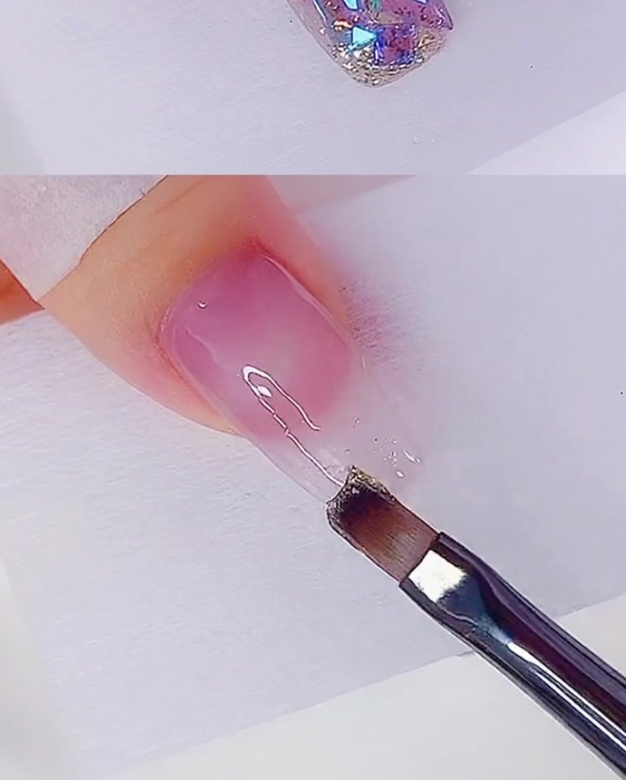 Un pincel plano aplicando una fina capa de gel con purpurina oro rosa en la punta de la uña.