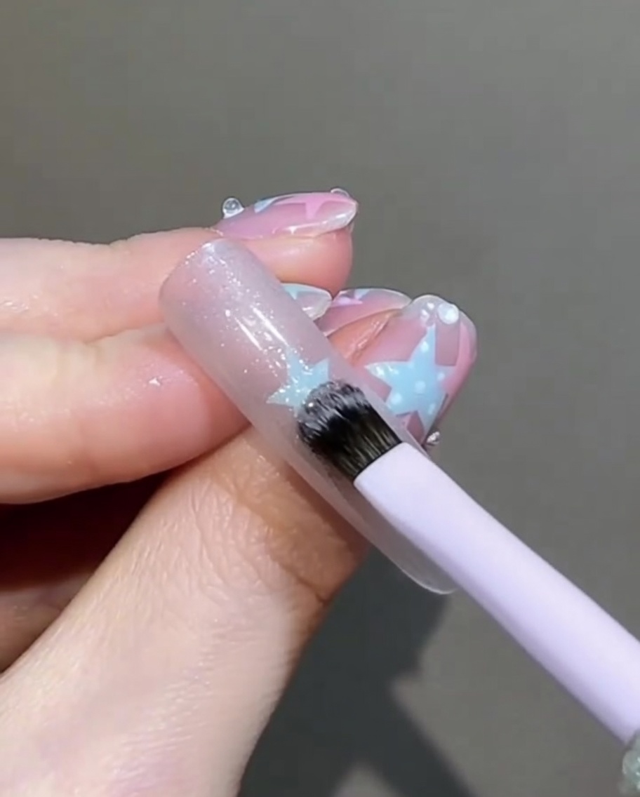 Un pequeño pincel plano dando suaves golpecitos y alisando la superficie del gel ojo de gato húmedo en la uña.