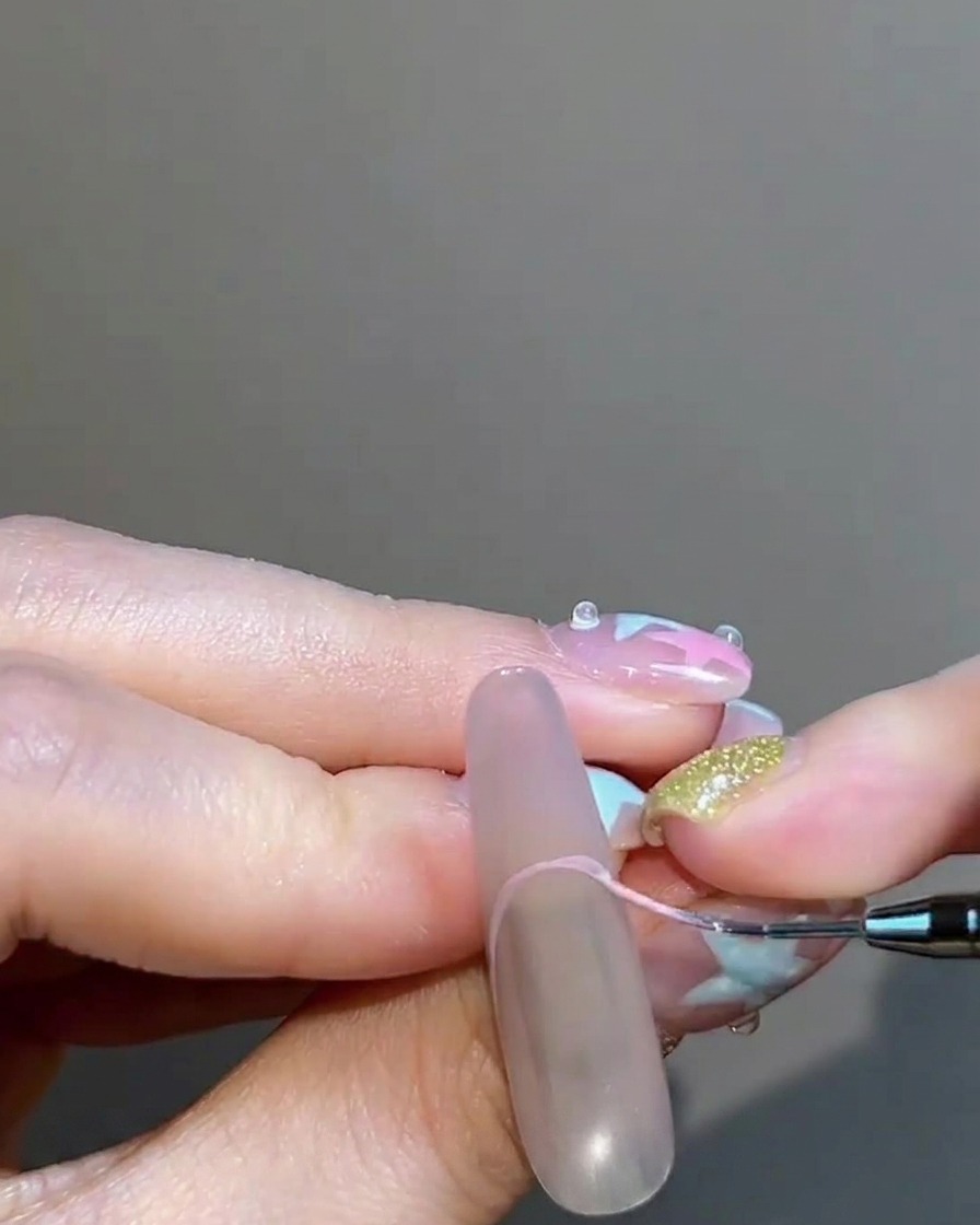 Un pincel delineador fino pintando cuidadosamente una punta francesa con gel en un tono nude rosado.