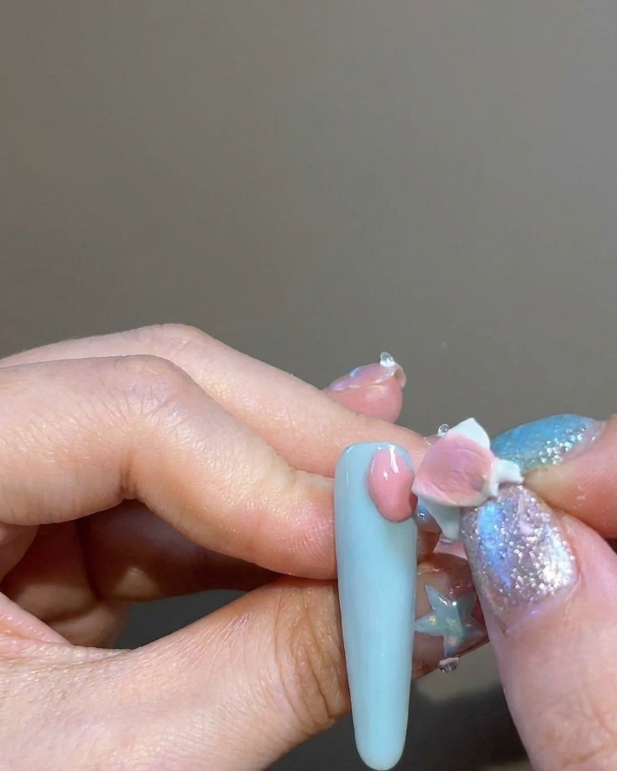 Un dedo usando una pequeña esponja para aplicar pigmento rosa sobre la uña alrededor de una pegatina en forma de cruz.