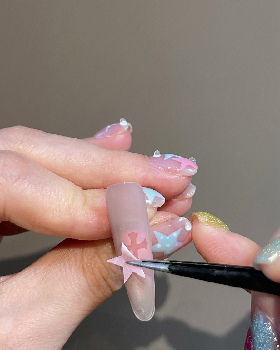 Unas pinzas despegando una pegatina de una uña, dejando una silueta transparente en forma de cruz en el centro del diseño aura.