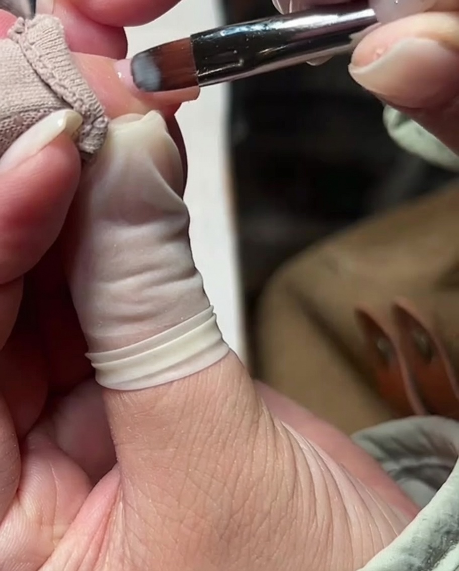 Un pincel de gel aplicando una capa fina de esmalte rosa nude sobre la superficie de la uña.