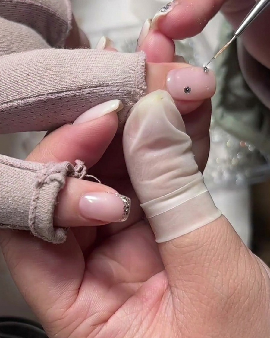 Un aplicador colocando un cristal sobre la base nude cerca de la cutícula.