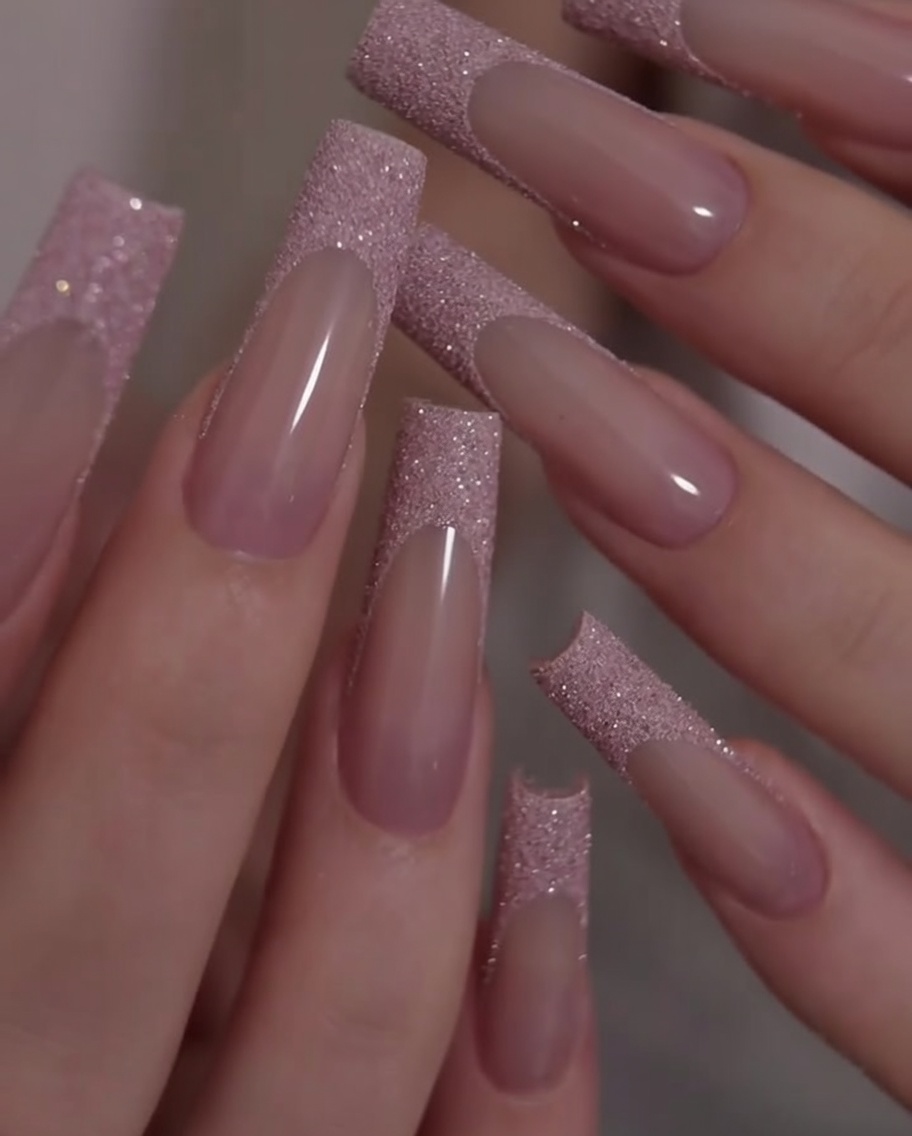 Primer plano de unas manos siendo rotadas para mostrar el contraste entre la base rosa y las puntas francesas de glitter.