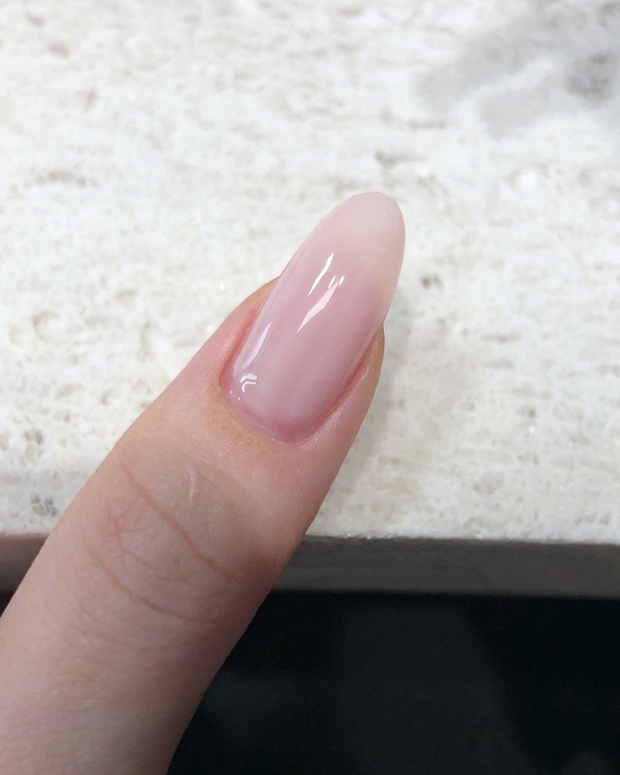 Vista cercana de una uña cubierta con un esmalte jelly nude rosado traslúcido con acabado liso.