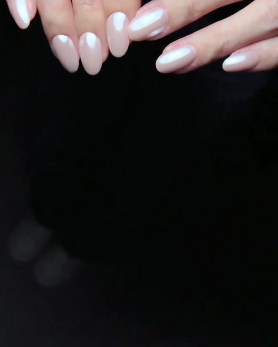 Uñas con dos capas de gel rosa curándose dentro de una lámpara LED.