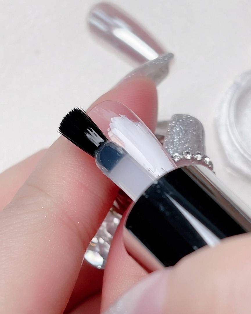 Un top coat transparente siendo aplicado con un pincel específicamente sobre la raya blanca central.