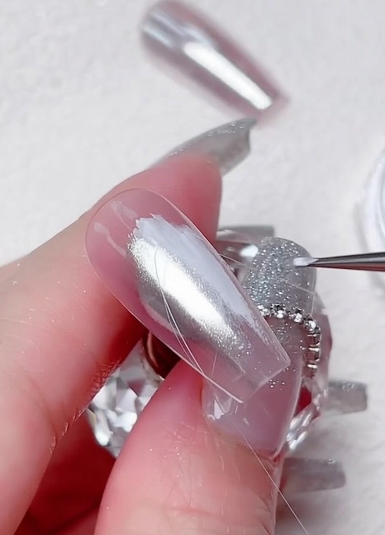 Un pincel liner dibujando líneas finas de gel transparente en patrón diagonal sobre la uña cromada.