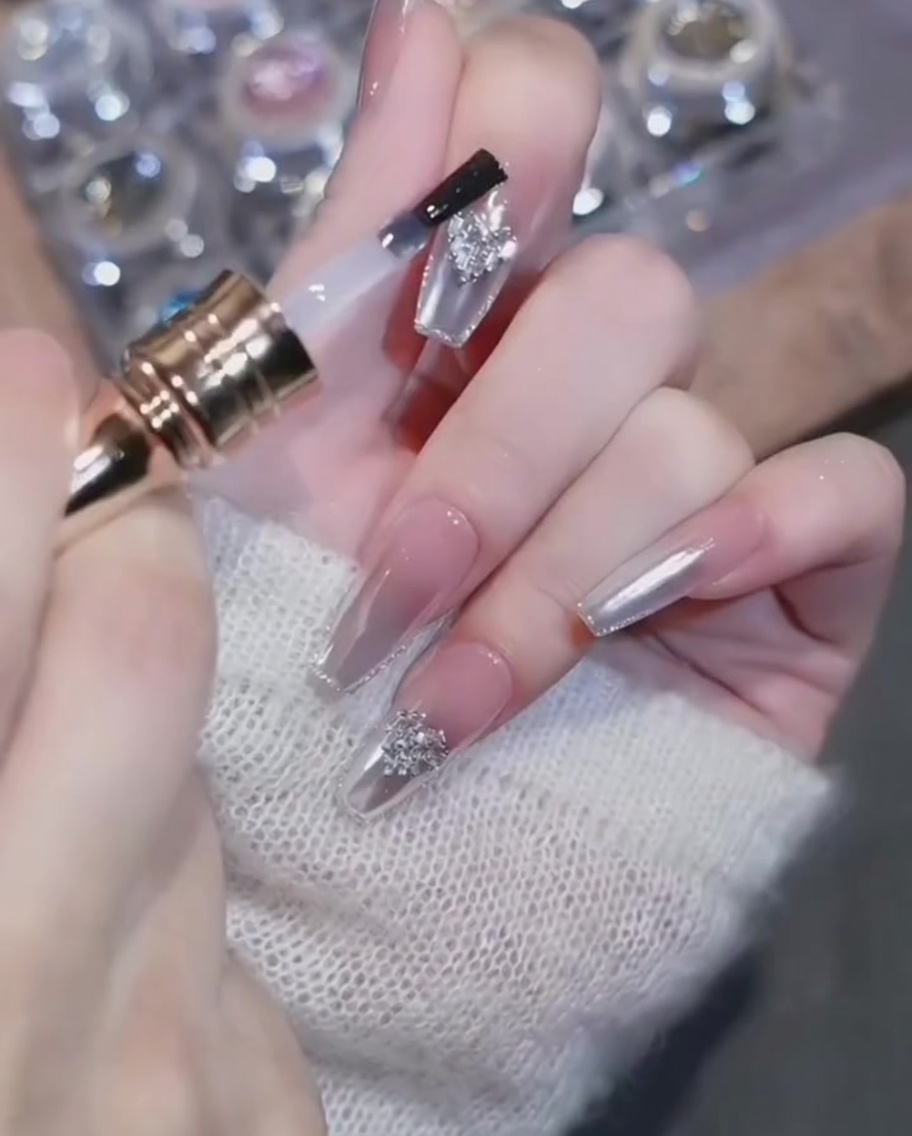 Un pincel de top coat aplicando gel cuidadosamente alrededor de un dije de corazón en una uña cromada terminada.