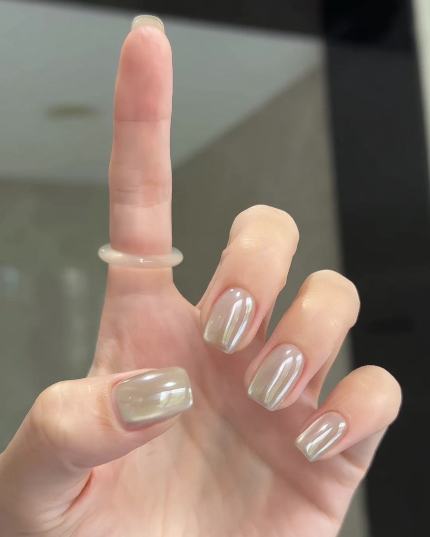 Un pincel suave frotando el polvo cromo perla sobre la superficie de las uñas para un acabado liso.