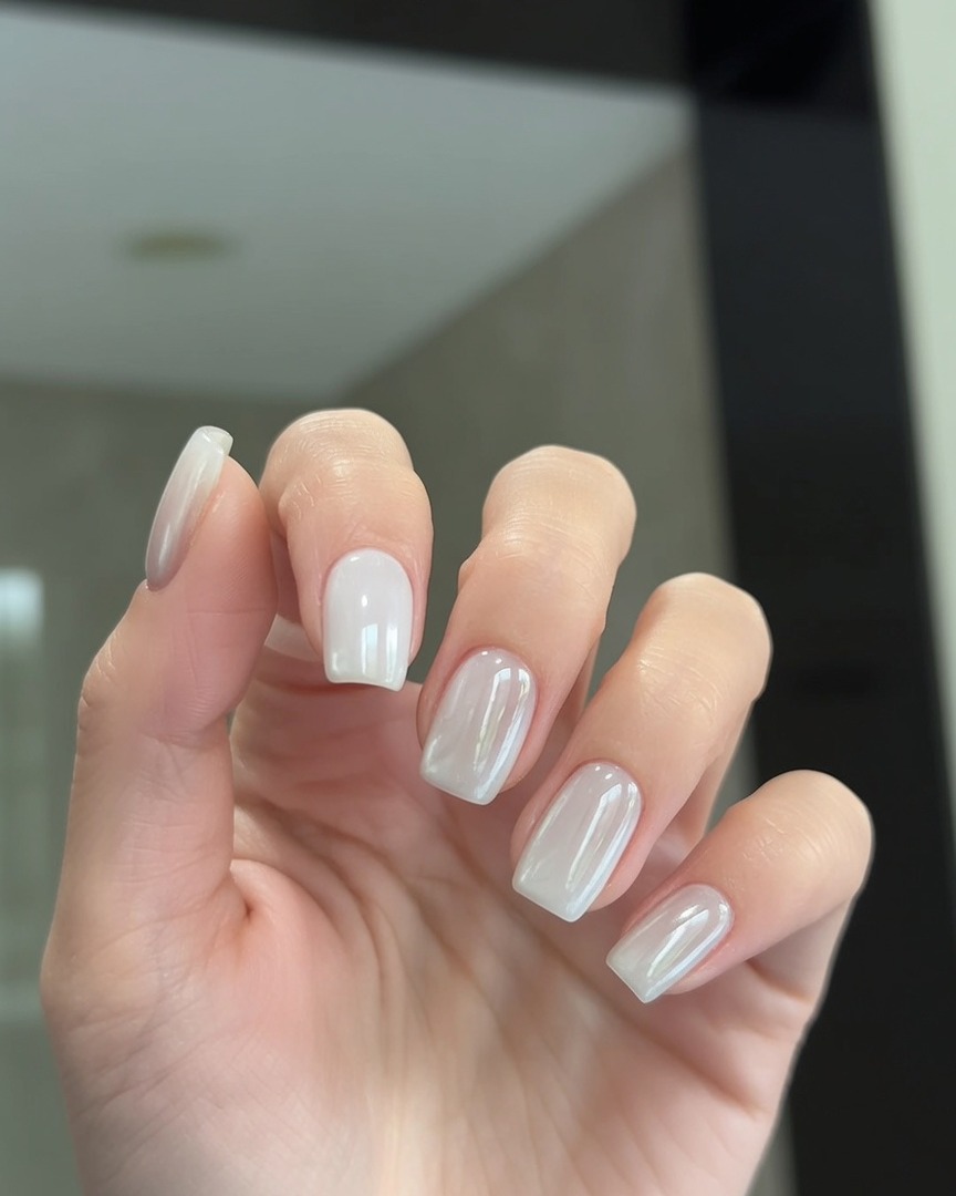 Un pincel aplicando una capa transparente de top coat sobre uñas con acabado cromo perlado.