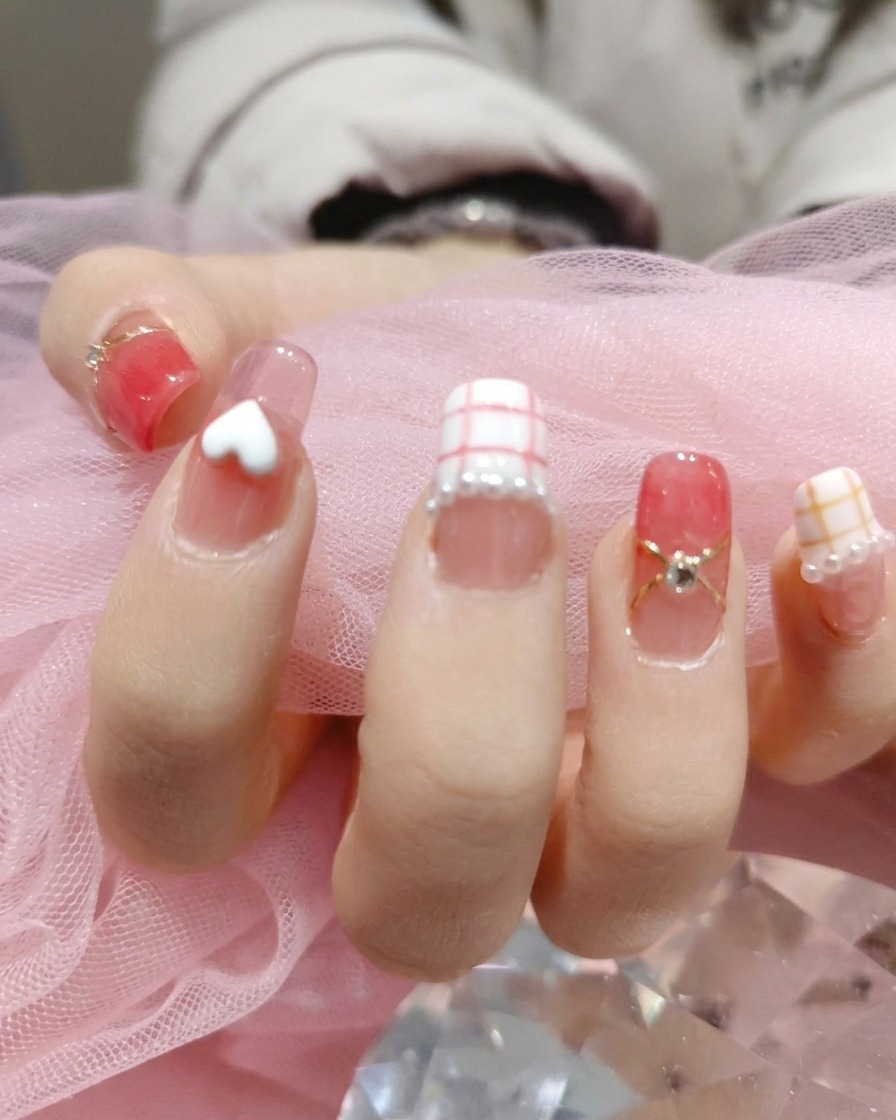 Una herramienta colocando diminutas perlas blancas iridiscentes alrededor de la base de los diseños de uñas en una mano manicurada.