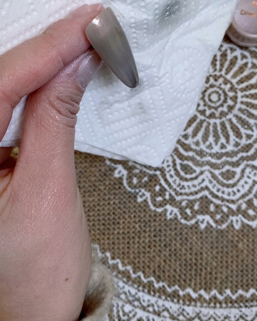 Primer plano de una punta de uña color gris sobre una servilleta de papel blanca.