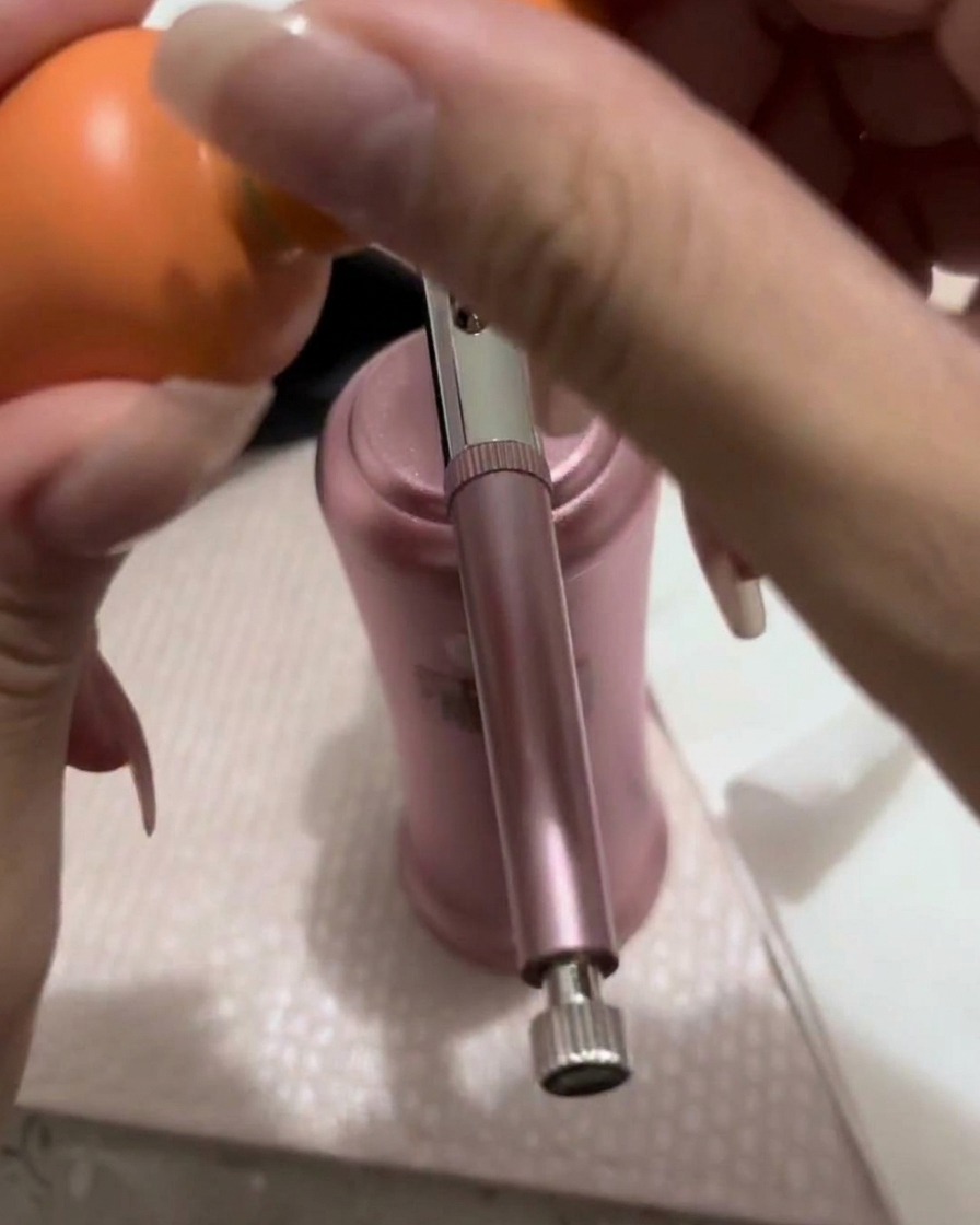 Una pequeña cantidad de gel color melocotón-rosa siendo transferida con un pincel a la copa metálica de un aerógrafo.