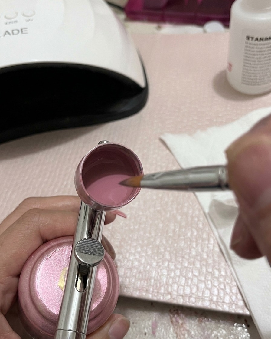 Primer plano de una herramienta de mezcla metálica revolviendo gel rosa dentro de la copa de un aerógrafo.
