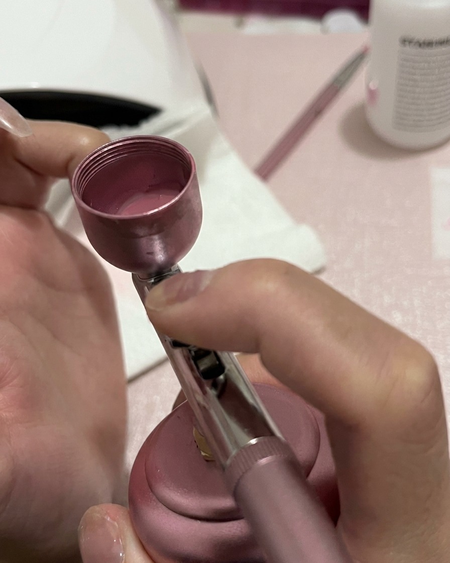 Primer plano de una uña recibiendo un spray más concentrado de pigmento rosa en la base y la sección media.