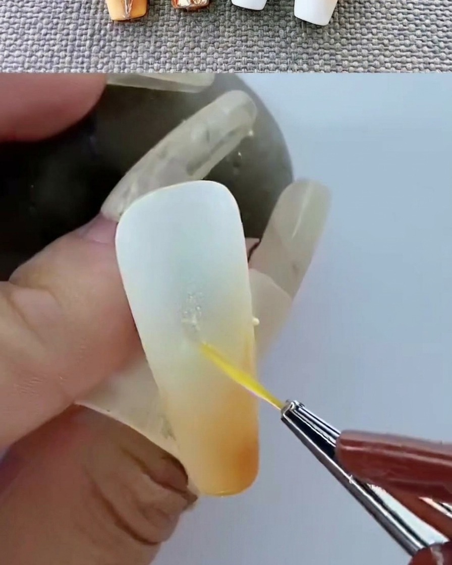 Pinzas colocando un emblema de metal dorado sobre una superficie de gel sin curar.
