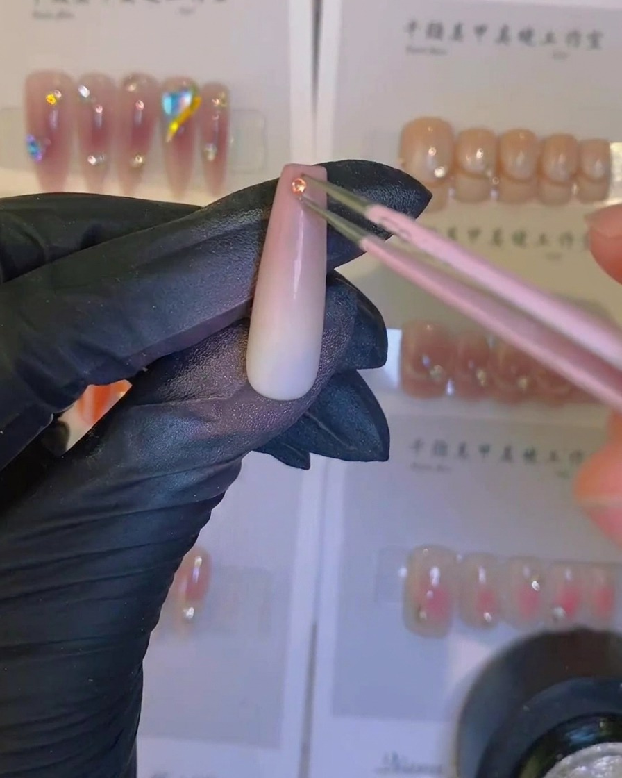 Un pincel aplicando un top coat transparente y brillante sobre una uña ombré con aerógrafo y un cristal.