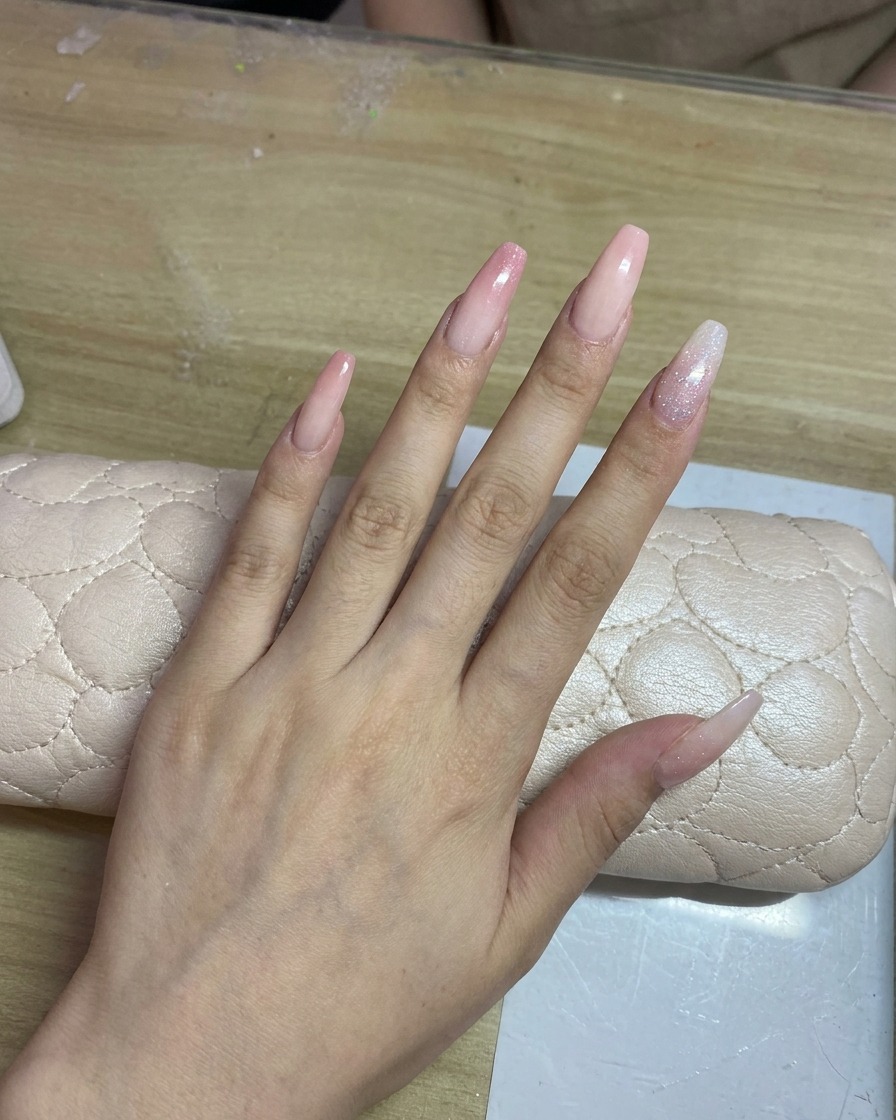 Una mano con uñas largas de tono claro recibiendo un delicado degradado rosa con aerógrafo.