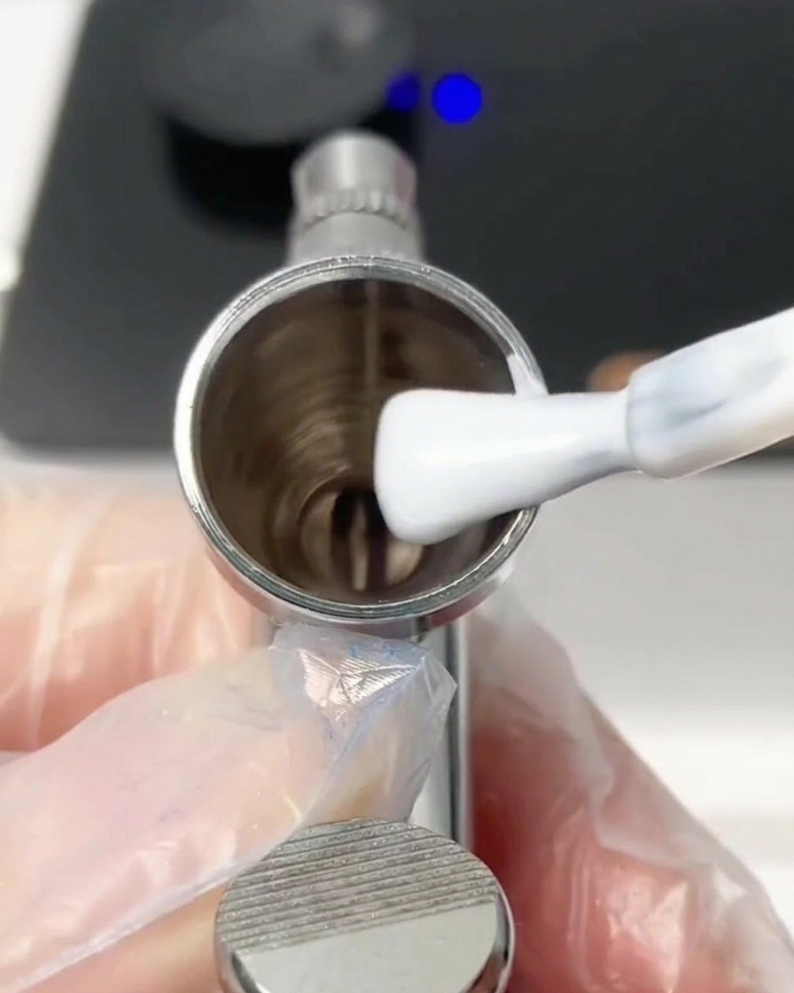 Un pincel colocando una gota de gel blanco dentro del depósito metálico del aerógrafo.