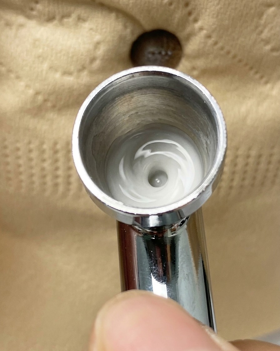 Un aerógrafo pulverizando una fina capa de pigmento blanco sobre un tip cubierto parcialmente con cinta.