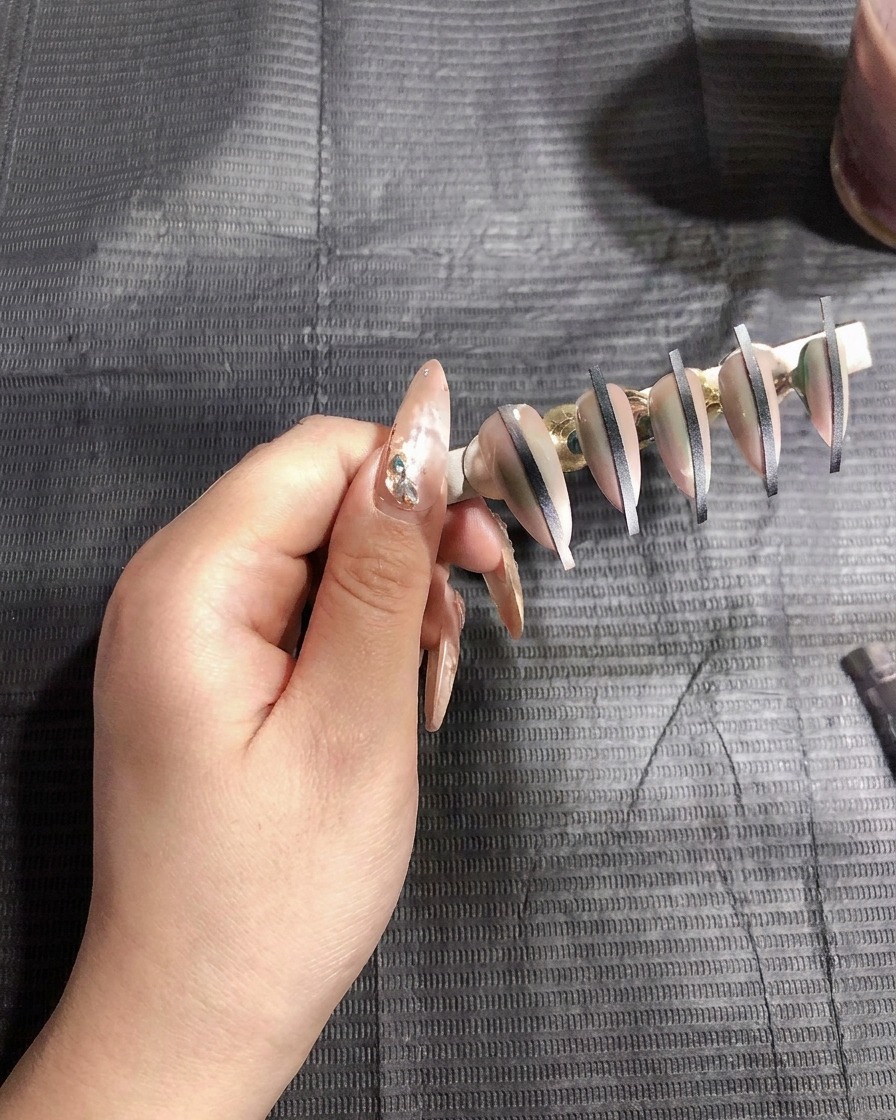 Un aerógrafo rociando una capa fina de gel blanco sobre uñas artificiales montadas en un soporte.
