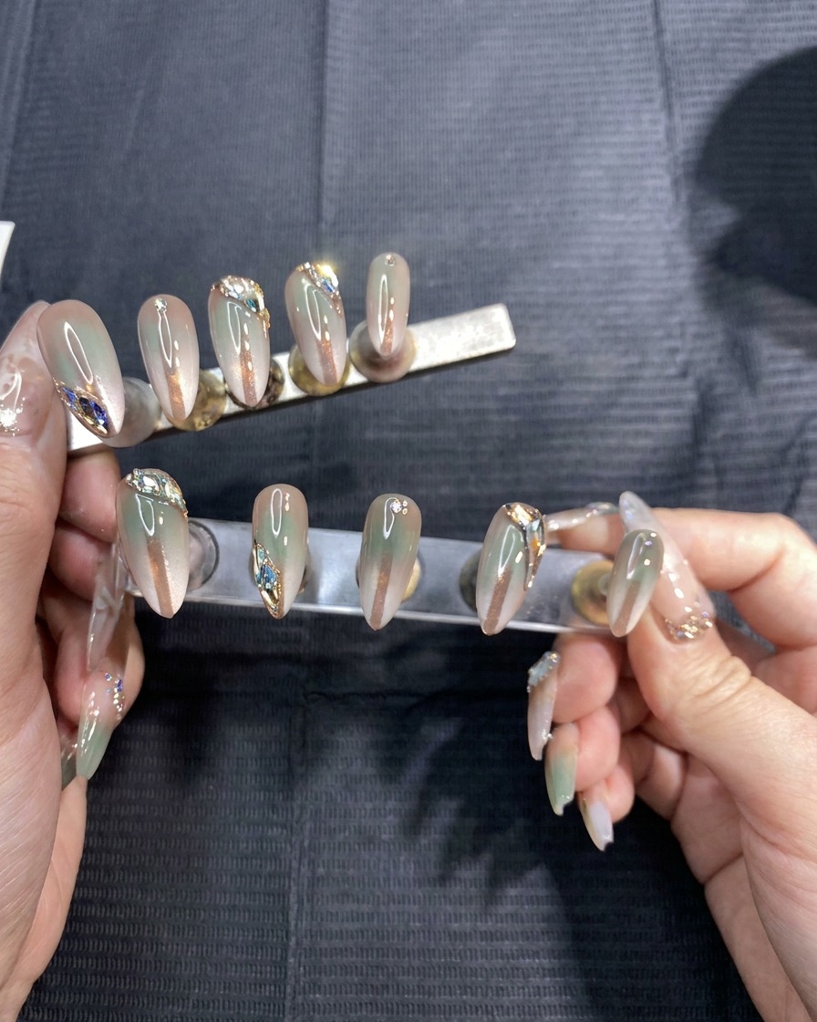 Un par de manos retirando cuidadosamente pegatinas de plantilla adhesivas de un set de uñas postizas pintadas con degradado.