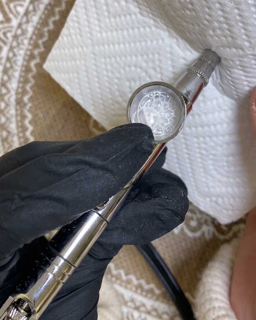 Un aerógrafo apuntando a una toalla de papel, mostrando un patrón de rociado de prueba de pintura blanca.