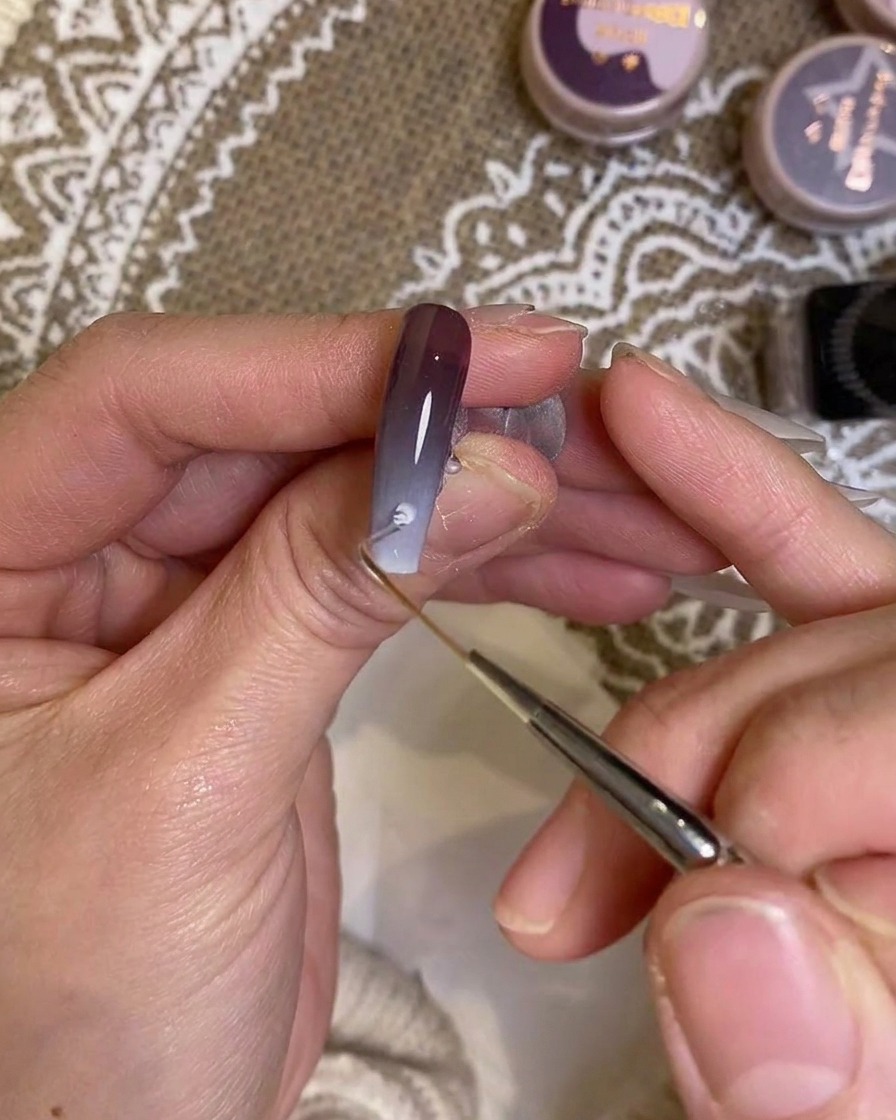 Un pincel de detalle aplicando cuidadosamente color cerca de la zona de la cutícula de la uña.