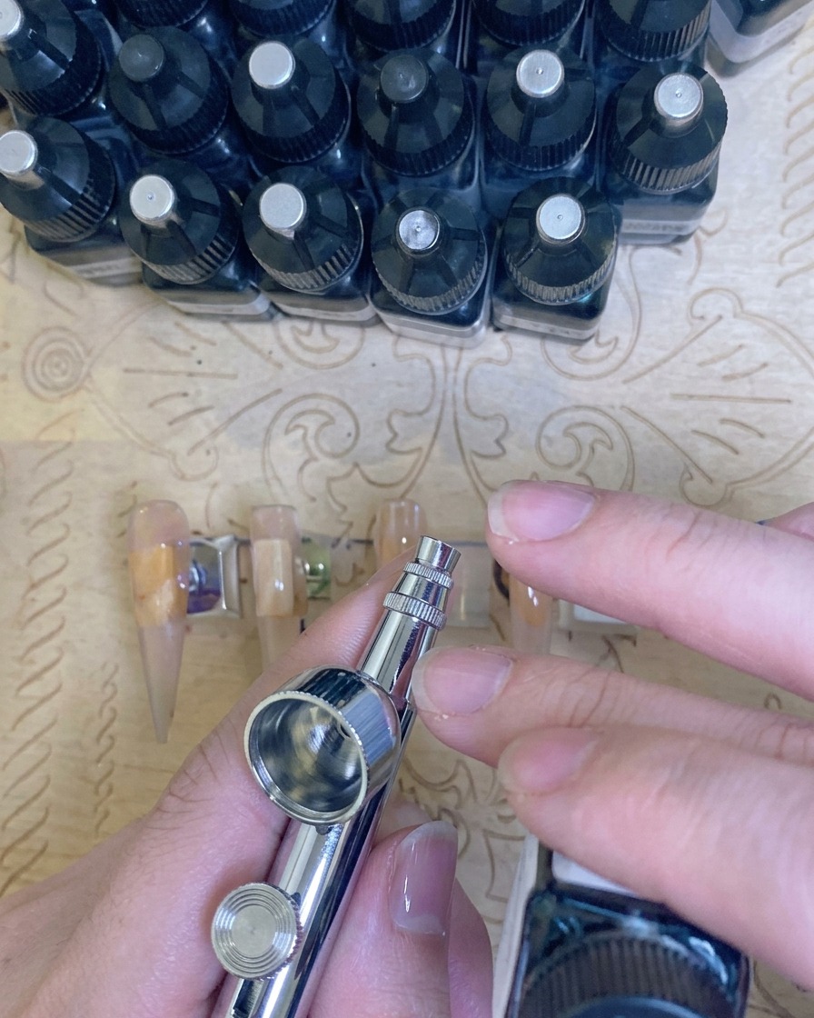 Vista de cerca de unos dedos colocados dentro de una lámpara UV/LED profesional con luz morada visible, curando la manicura.