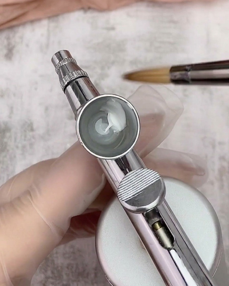 Vista dentro de una copa de aerógrafo que contiene una mezcla de gel blanco y diluyente, con un pincel al fondo.