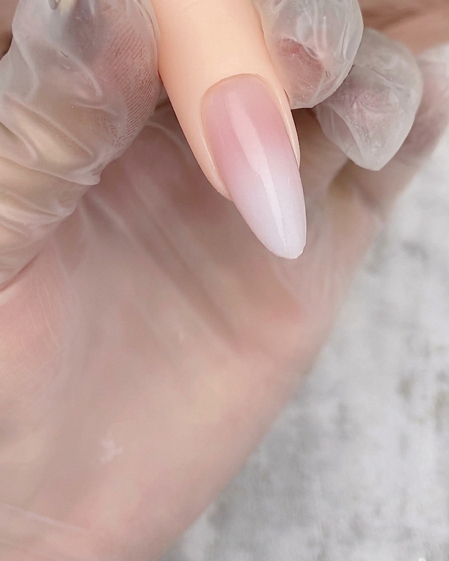 Uña en forma de almendra mostrando un suave degradado blanco traslúcido aplicado sobre una base nude.