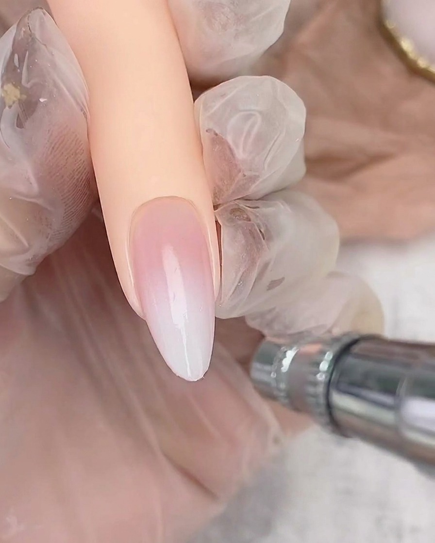 Aerógrafo rociando ligeramente esmalte blanco sobre el borde libre de una uña almendrada para crear el efecto ombré.